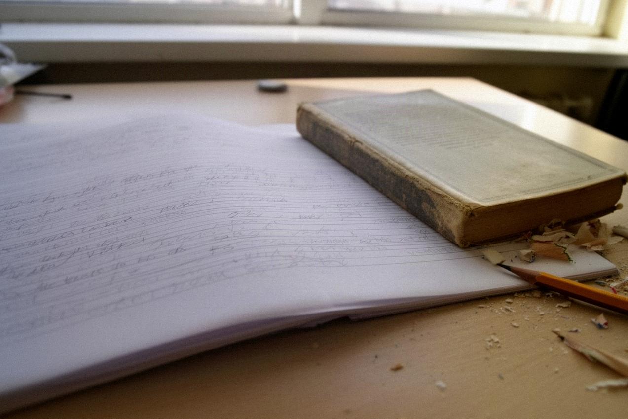 Zeszyt z odręcznym planem w punktach obok zamkniętej książki na biurku ucznia