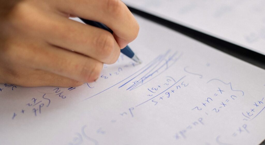 Dłoń zapisująca rozwiązanie zadania matematycznego na kartce